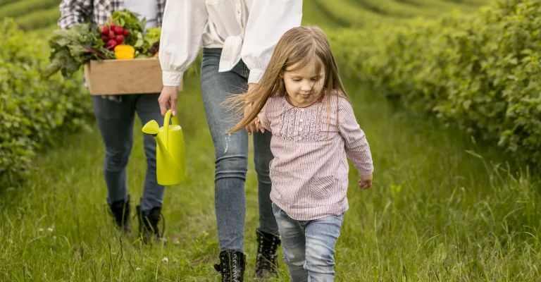 Mamă și fetiță pe o alee dintre culturi, cu o ladă de legume proaspăt culese