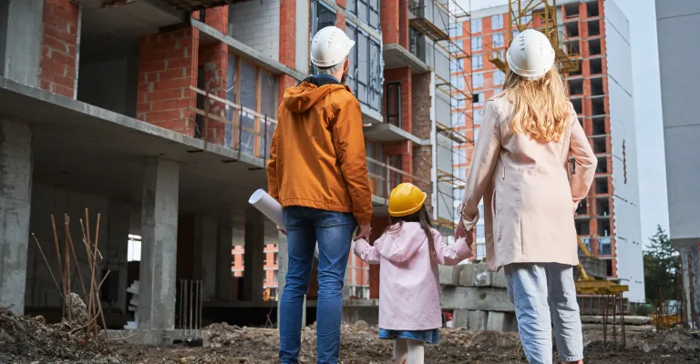 Familie cu căști de protecție în fața unui bloc în construcție