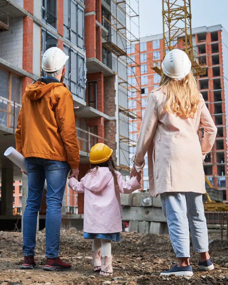 Familie cu căști de protecție în fața unui bloc în construcție